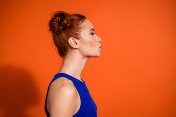 Obraz premium Profile portrait of a woman with red hair and bun hairstyle against vibrant orange background in stylish blue top with casual expression