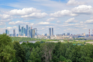Breathtaking view of Moscow skyline from Vorobyovy Gory, with Moscow River, green trees, and clouds in the blue sky. The Moscow skyline dominates the horizon, creating a stunning scene