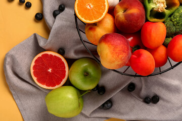 Basket with different fresh fruits and vegetables on yellow background, closeup