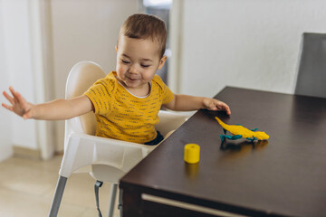 Two-year-old toddler sitting in a high chair, playing and interacting with his mother, sharing a...