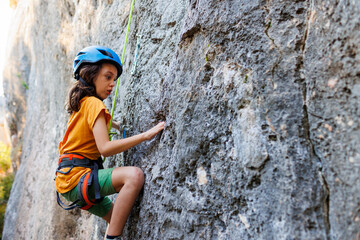 boy climber in a helmet. A determined and strong boy climber climbs a steep mountain wall. A child...