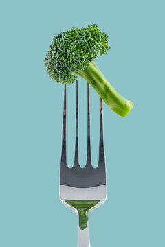 Fresh broccoli floret impaled on fork against teal background: promoting healthy eating habits