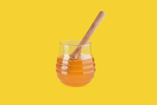 Honey dripping from wooden honey dipper into glass jar on yellow background - Powered by Adobe