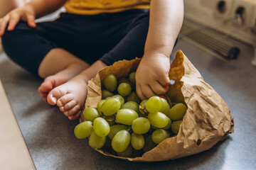 Close up of children feet next to a paper bag filled with grapes, capturing a warm and natural moment