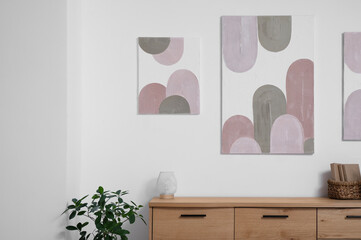 Interior of stylish room with wooden dresser, houseplant and pictures on white wall