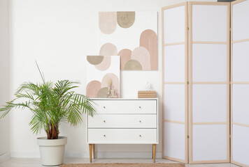 Stylish room with chest of drawers, houseplant and picture on white wall