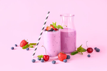 Glass and bottle of fresh smoothie with different berries on pink background