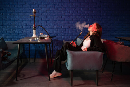 Relaxed young woman enjoying hookah in modern lounge setting