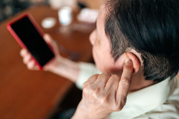 Close-up of a senior person inserting a modern hearing aid behind their ear, highlighting assistive...
