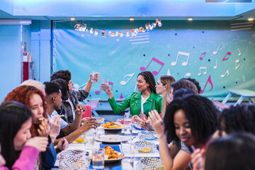Group of diverse friends enjoying a meal and toasting drinks together in a bowling alley restaurant