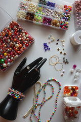 Hand figurine, colorful friendship bracelets, necklaces, various beads and DIY supplies on the table. Making jewelry at home. Flat lay.