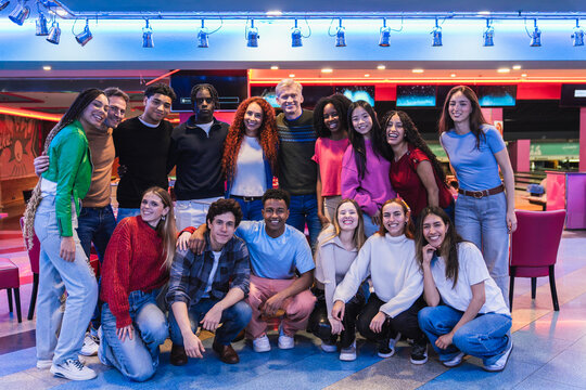 Happy multi ethnic friends posing together, having fun at the bowling alley and arcade video game room