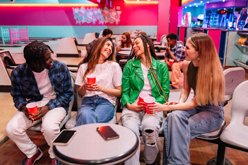 Group of diverse friends enjoying drinks and conversation while sitting together in a bowling alley