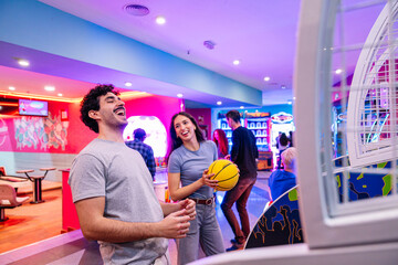Young adults having fun playing arcade basketball game in entertainment center with neon lights