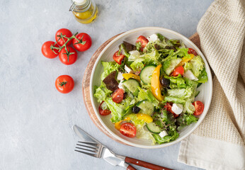 Fresh vegetable salad with feta cheese and olives on plate on a light background.