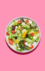 Vegetable salad with lettuce, vegetables, olives and feta cheese on bright pink background