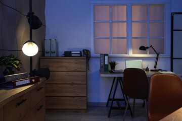 Interior of dark office with workplace, drawers and glowing lamps
