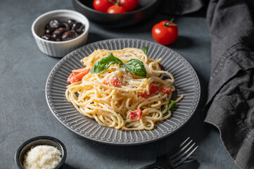 Creamy spaghetti with cherry tomatoes, parmesan cheese and basil on a plate on a dark background
