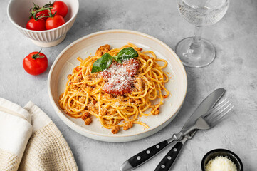 Spaghetti bolognese with tomato sauce, basil and parmesan cheese on a plate on a gray background