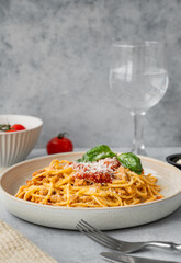 Spaghetti bolognese with tomato sauce, basil and parmesan cheese on a plate on a gray background