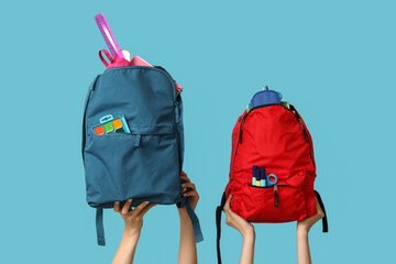 Female hands with different backpacks and school supplies on blue background, closeup
