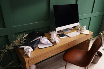 Messy workplace with modern computer, garbage and papers near green wall in office