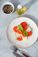 Caprese salad with sliced ​​tomatoes, mozzarella and basil on a plate on a light background