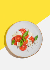 Fresh Caprese salad with tomatoes, mozzarella and basil on a white yellow background.