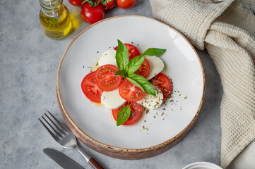 Caprese salad with sliced ​​tomatoes, mozzarella and basil on a plate on a light background