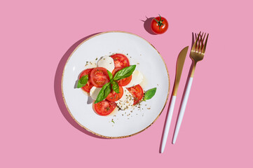 Caprese salad with fresh tomatoes, mozzarella and basil on pink background.