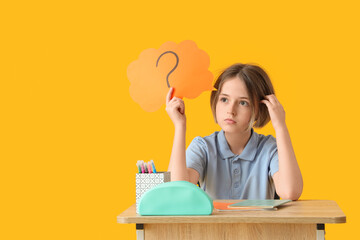 Thoughtful schoolboy with stationery and speech bubble sitting on desk against yellow background