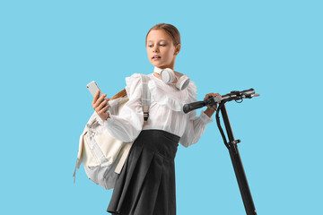 Cute schoolgirl with headphones, mobile phone and electric scooter on blue background © Pixel-Shot