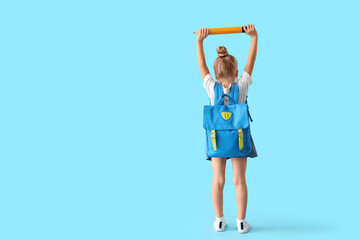 Cute little schoolgirl with big pencil and backpack on blue background, back view