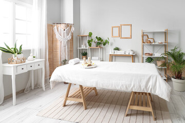 Interior of light spa salon with massage couch, shelf units and tables