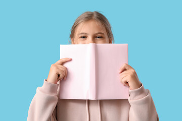 Cute schoolgirl with book on blue background