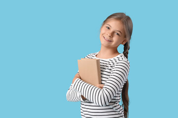 Cute schoolgirl with book on blue background