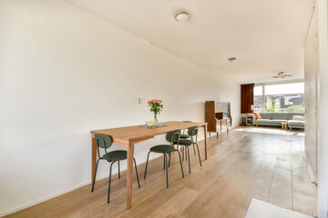 A sleek and modern dining area featuring a wooden table with chairs, illuminated by natural light from large windows, exuding a minimalistic aesthetic.