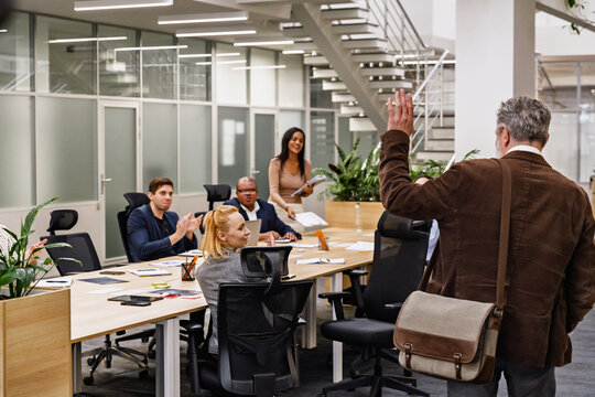 A White elderly employee bids farewell to his diverse coworkers by waving goodbye after a meeting in an office, as they smile at him. A concept of respect and positive relationships among colleagues.