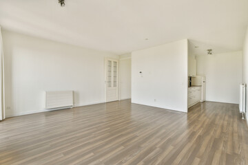 A spacious, modern empty room featuring light-colored walls and a wooden floor, complemented by an open kitchen area. Ideal for interior design exploration.