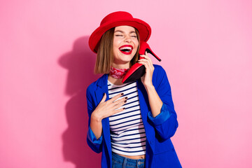 Stylish young woman in vibrant outfit holding a red shoe to her ear as a phone, expressing joy and...