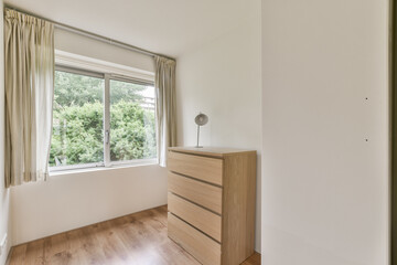 Bright and airy room featuring a wooden dresser and large window overlooking greenery, embodying a...