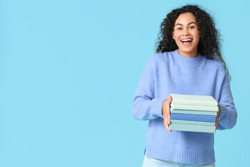 Happy young African-American woman with with stack of books on blue background