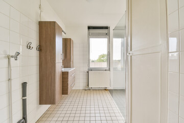Bright, airy bathroom featuring white tiles, wooden cabinets, and a large window that enhances natural light, creating a clean and spacious ambiance.
