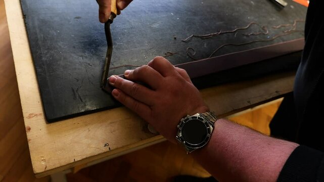 Leatherworker using swivel knife to carve edges of leather belt in workshop
