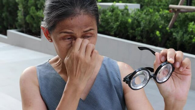 Unhappy old Asian senior woman, grandma with poor vision of real aged elderly person looking through the eyeglasses lens with frustration and unhappiness