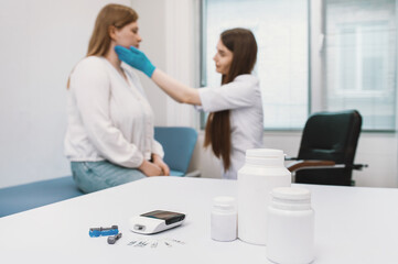 Fototapeta premium An endocrinologist at a reception with a patient conducts an examination of the lymph nodes and thyroid gland by palpation. Tablets and a glucometer are in the foreground