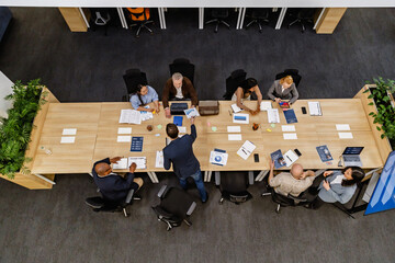 A top-down view of a diverse group of business colleagues working around a long conference table....