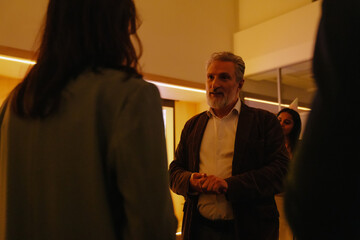 A serious gray-haired European man in his early 50s with a beard dressed in a dark jacket talking...