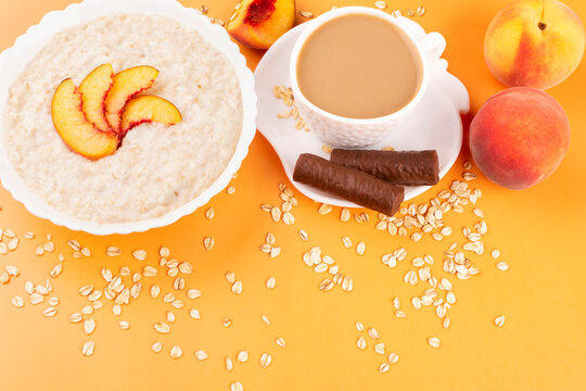 Milk oatmeal porridge with a peach in a white plate and a cup of coffee on an orange background. Healthy breakfast. Space for the text.