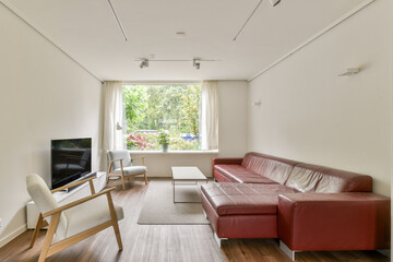 A stylish modern living room featuring a red leather sofa, minimalist furniture, and large windows allowing natural light to flood in, creating a welcoming atmosphere.